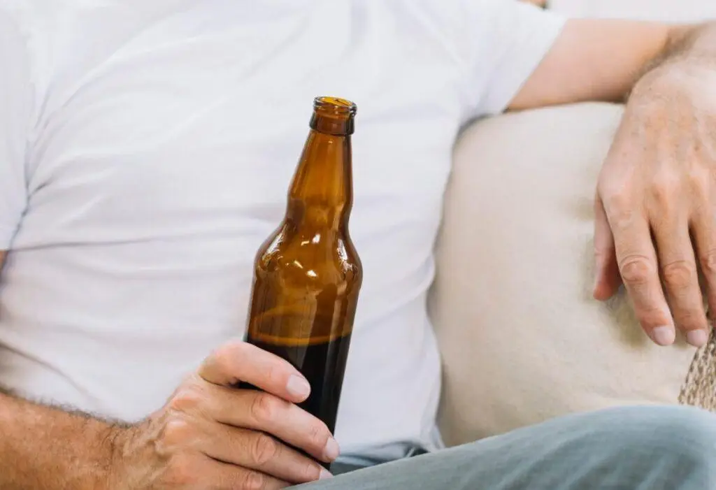 mezczyzna siedzacy na kanapie z butelka piwa w rece uzaleznienie od alkoholu