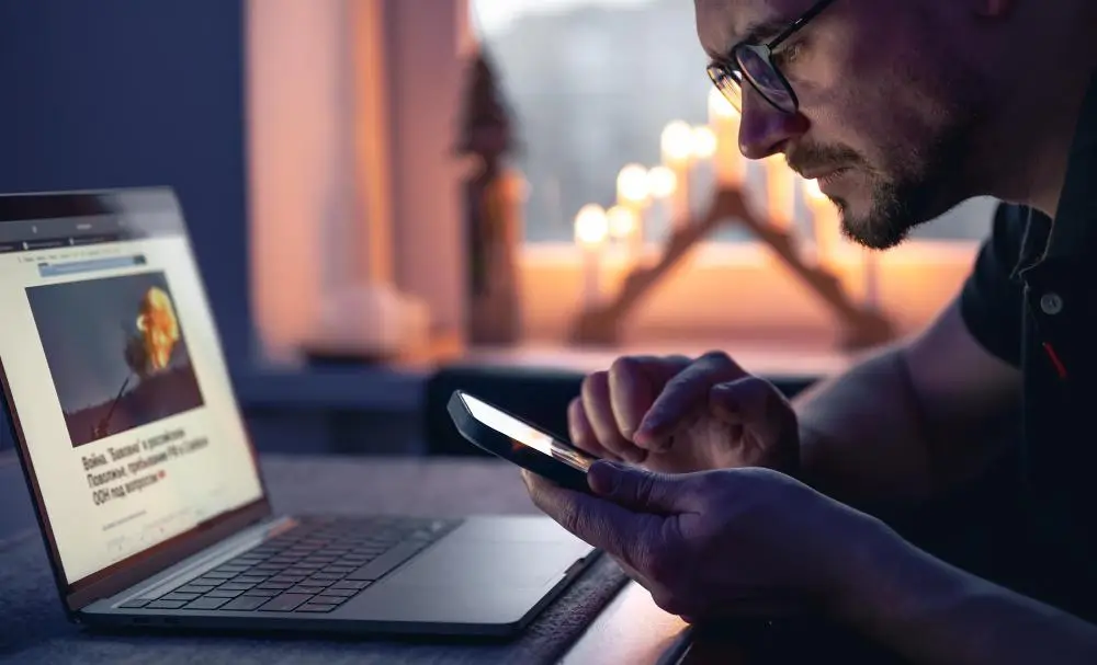 mezczyzna patrzacy na ekran laptopa trzymajac telefon w dloni analizujacy informacje w centrum optimus