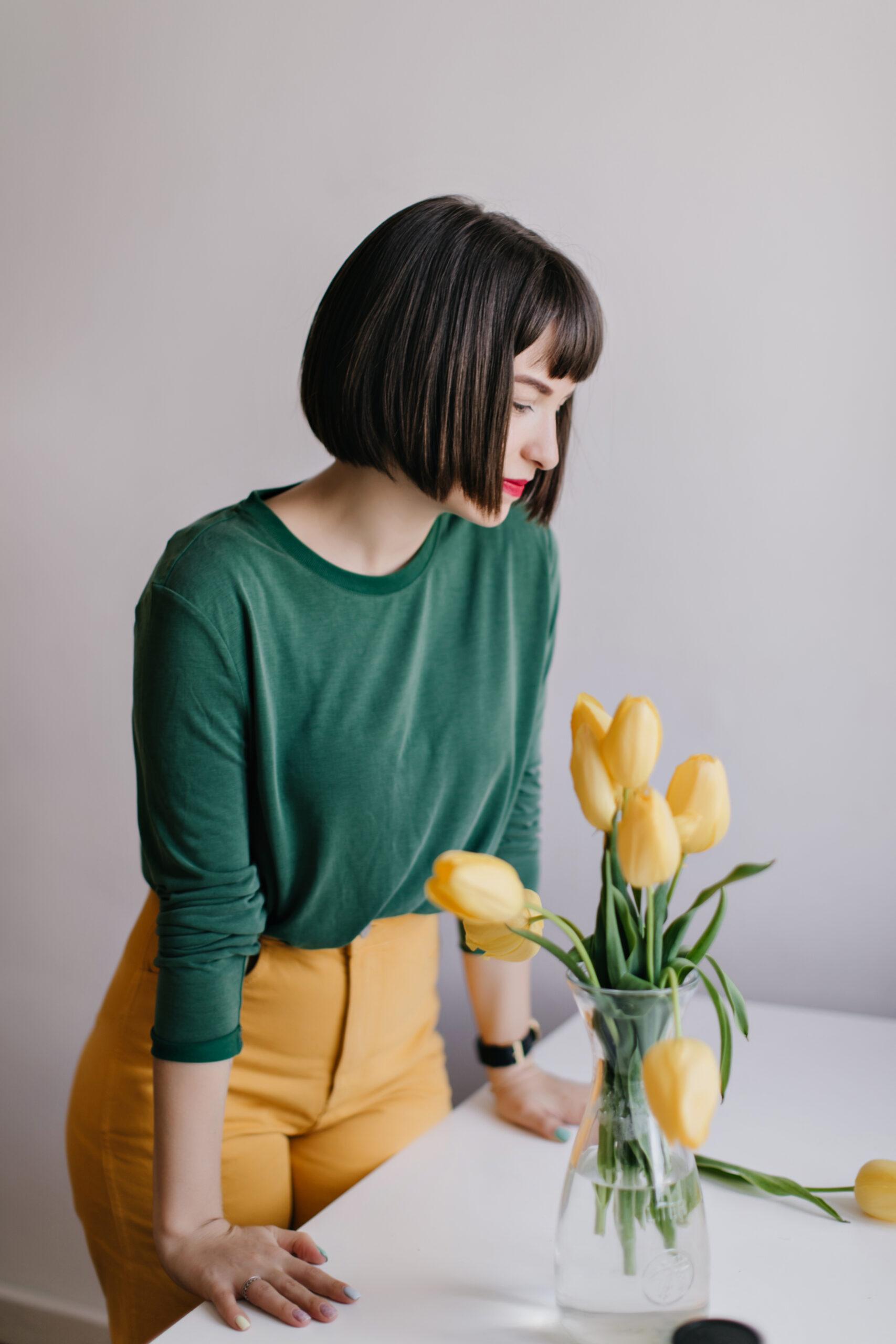 mloda kobieta stojaca przy stole i patrzaca na zolte tulipany