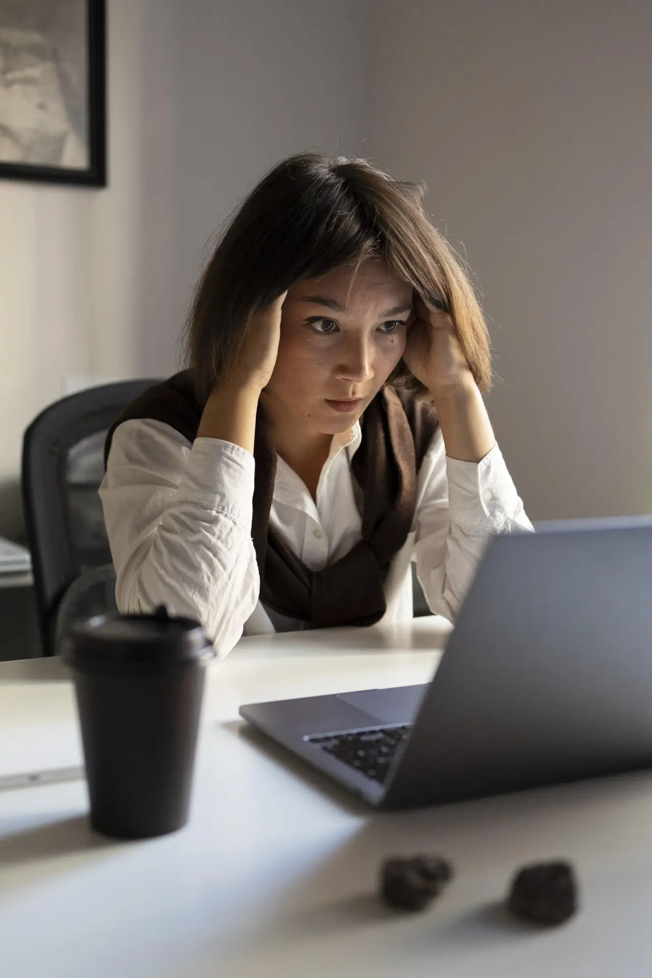 sfrustrowana kobieta przy biurku trzymająca dłonie przy skroniach podczas pracy przy laptopie jako obraz trudności z koncentracją w ADHD