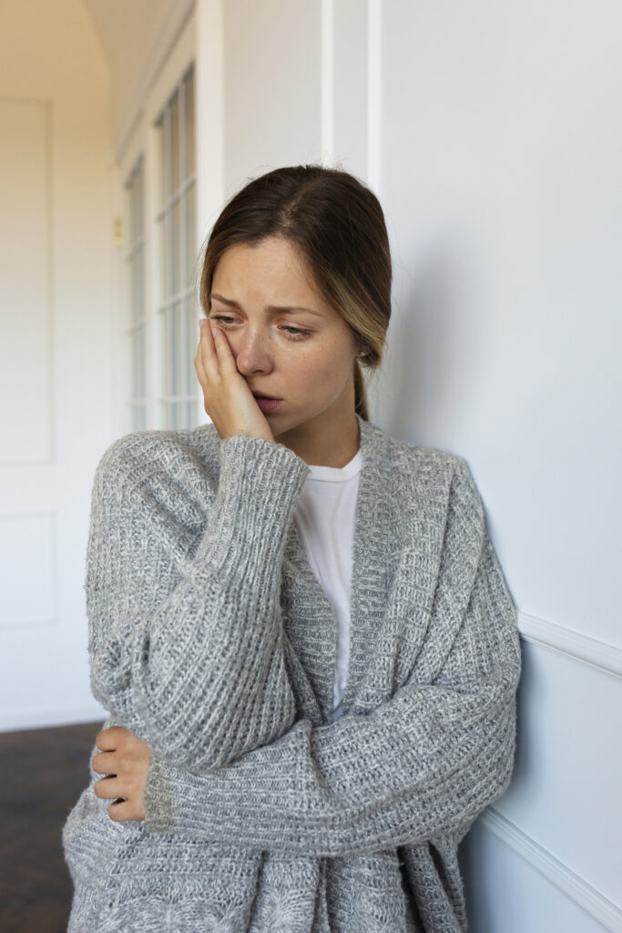 zmartwiona kobieta stojąca przy ścianie w pomieszczeniu