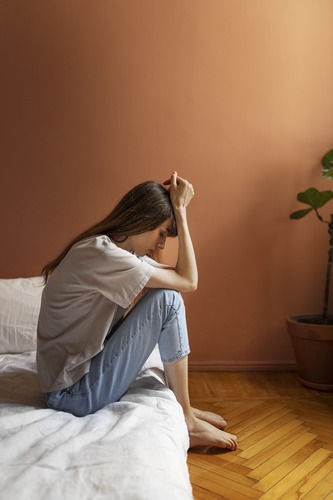 Kobieta w kryzysie emocjonalnym siedząca na łóżku w domu
