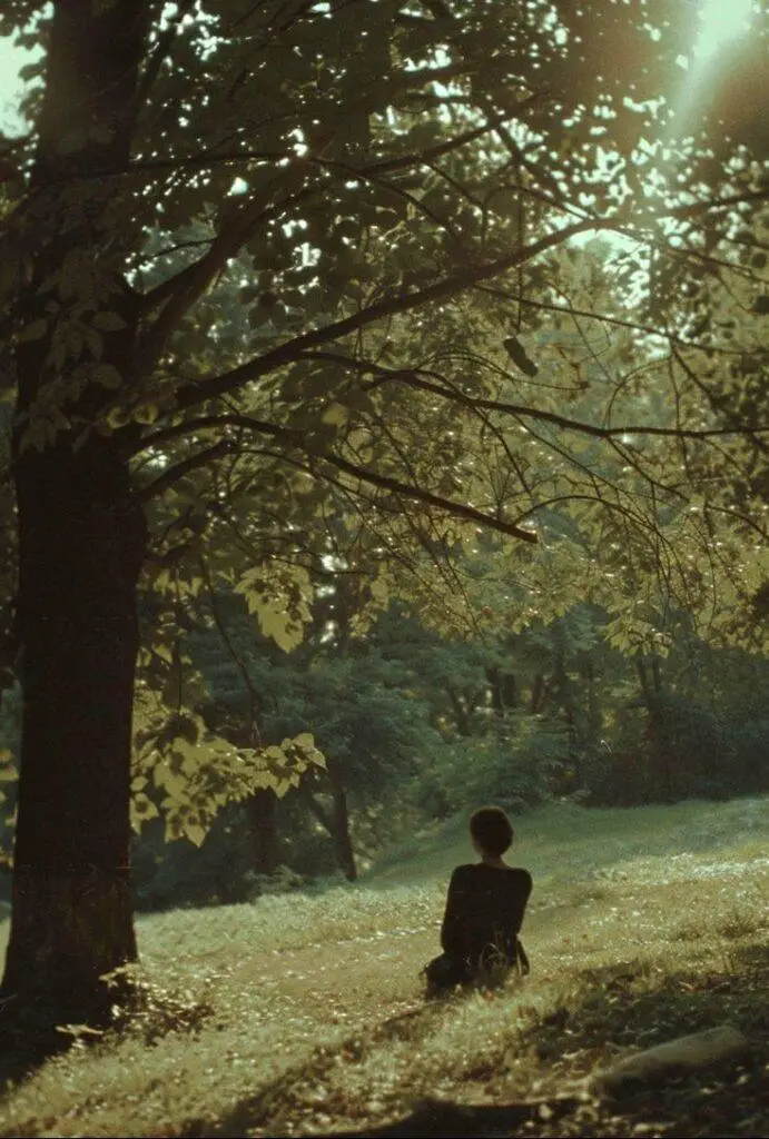 Osoba siedząca samotnie w parku pod drzewem, w spokojnej, refleksyjnej atmosferze