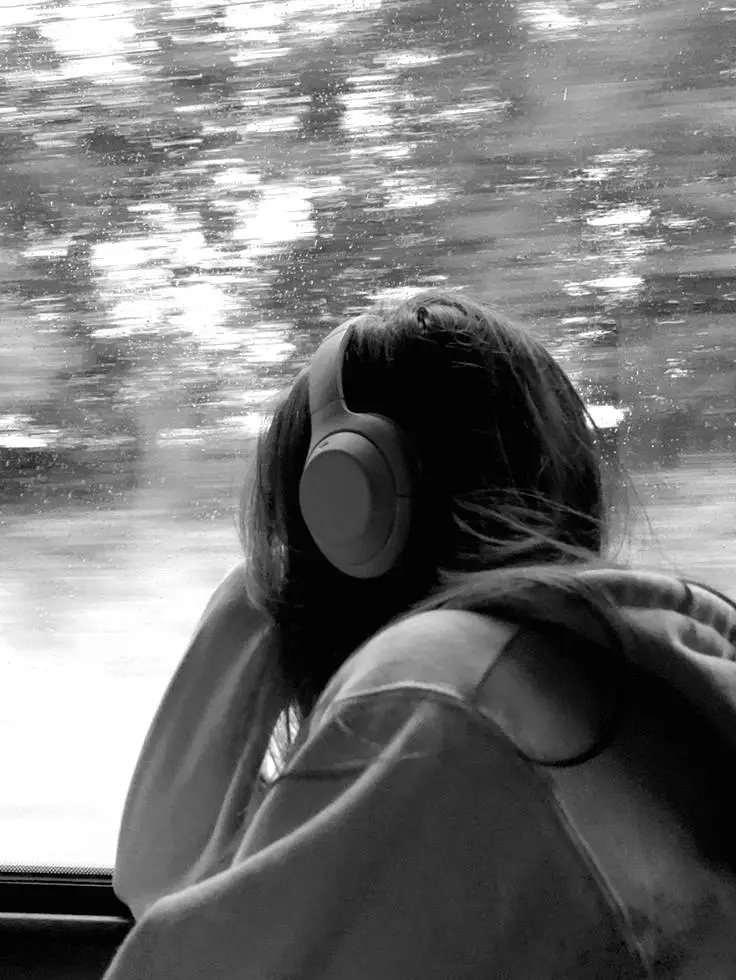 Osoba siedząca przy oknie w słuchawkach, zamyślona, obserwująca krajobraz za szybą