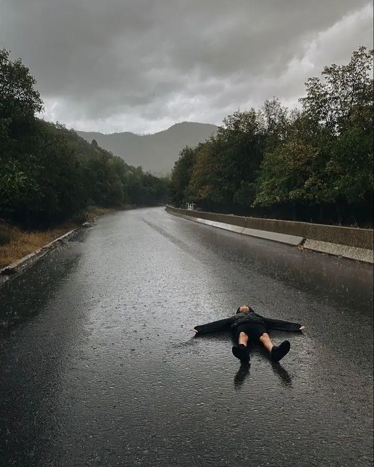 Osoba leżąca na mokrej drodze w deszczu, wyrażająca bezsilność i przeciążenie emocjonalne