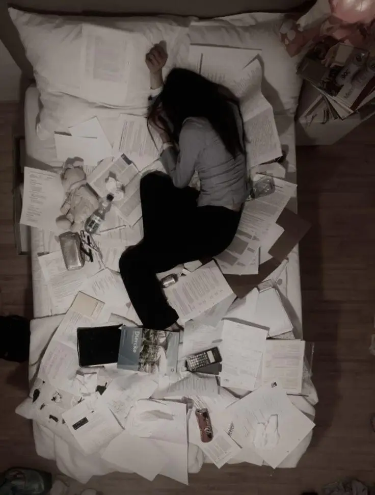 Kobieta leżąca wśród porozrzucanych notatek i telefonu, przytłoczona i zmęczona